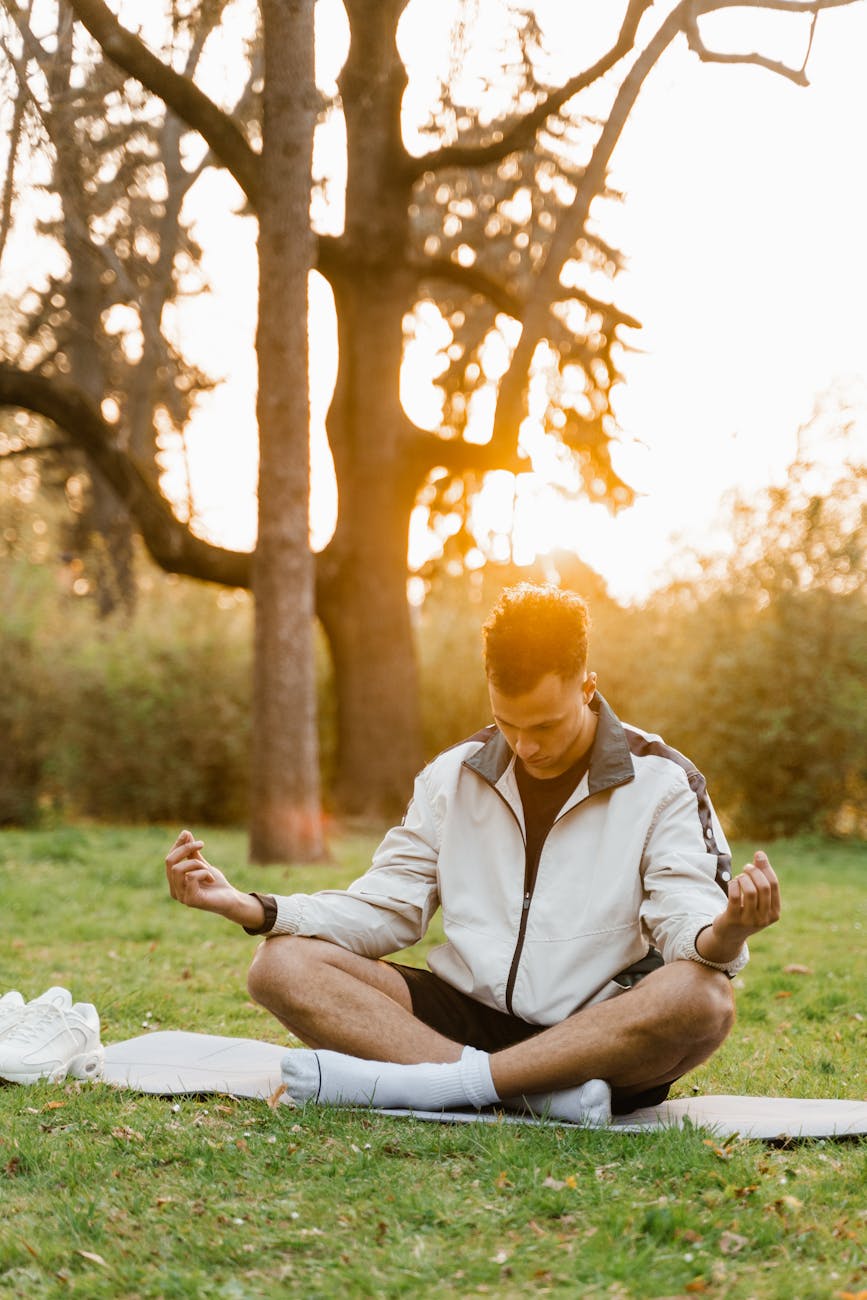 a young man meditating in white jacket sitting on a mat on park